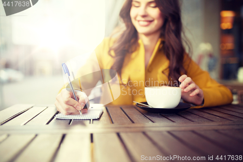 Image of happy woman with notebook and cappucino at cafe