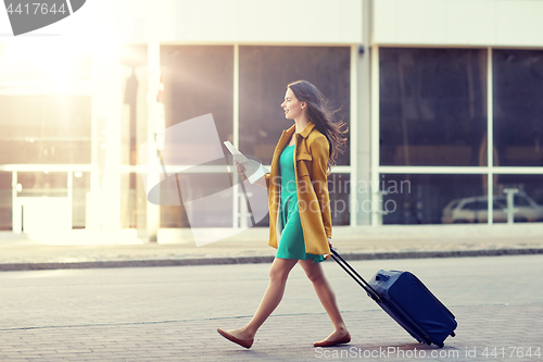 Image of happy young woman with travel bag and map in city