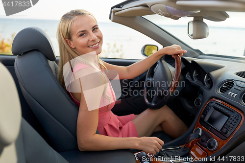 Image of happy young woman driving convertible car