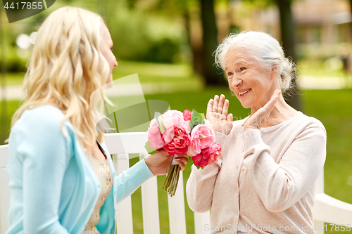 Image of daughter giving flowers to senior mother at park