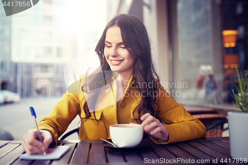 Image of happy woman with notebook drinking cocoa at cafe