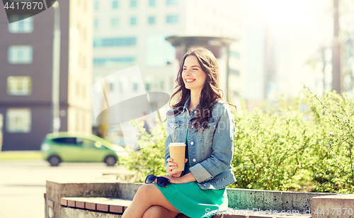 Image of happy young woman drinking coffee on city street