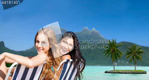 Image of happy women sunbathing in chairs on exotic beach