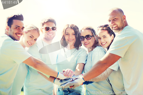 Image of group of volunteers putting hands on top in park