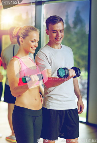 Image of smiling young woman with personal trainer in gym