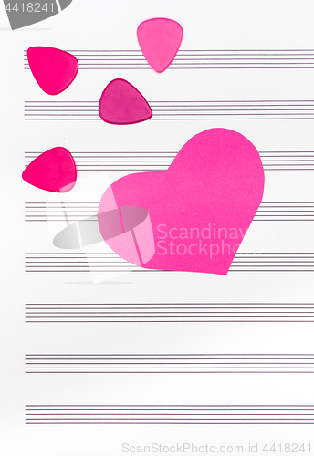 Image of Pink heart and guitar picks on empty sheet music paper