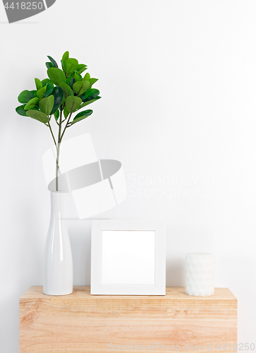 Image of Stylish decor with white picture frame, ficus leaves and candle