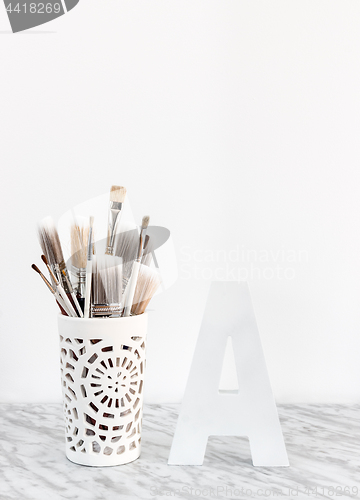 Image of Paintbrushes in a decorative vase and letter A on marble surface