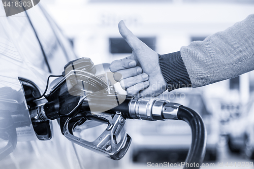 Image of Petrol or gasoline being pumped into a motor vehicle car. Closeup of man, showing thumb up gesture, pumping gasoline fuel in car at gas station.