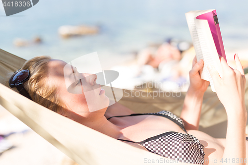 Image of Woman reading book in hammock on the beach