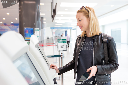 Image of Casual caucasian woman using smart phone application and check-in machine at the airport getting the boarding pass.