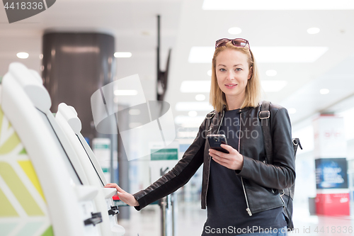 Image of Casual caucasian woman using smart phone application and check-in machine at the airport getting the boarding pass.