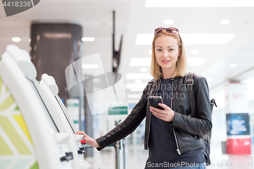 Image of Casual caucasian woman using smart phone application and check-in machine at the airport getting the boarding pass.