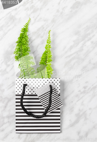 Image of Green fern branches in a gift bag on marble background