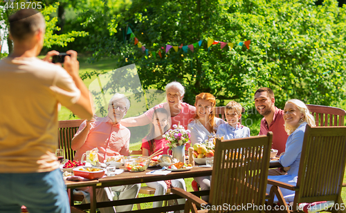 Image of happy family photographing at dinner in garden