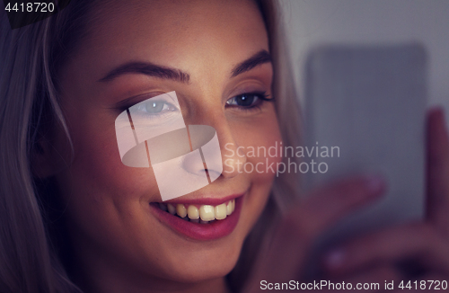 Image of happy smiling young woman with smartphone at night