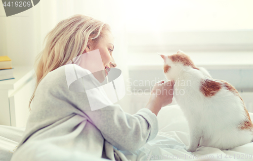 Image of happy young woman with cat in bed at home