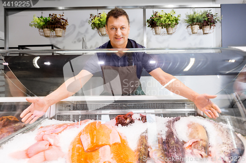 Image of male seller showing seafood at fish shop fridge