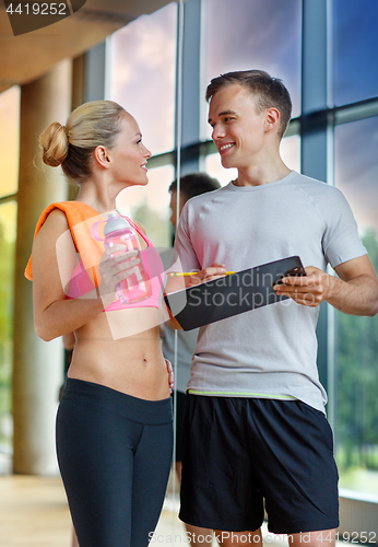 Image of smiling young woman with personal trainer in gym