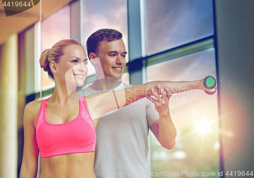 Image of smiling young woman with personal trainer in gym