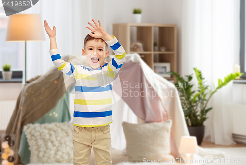 Image of happy little boy waving hands at home