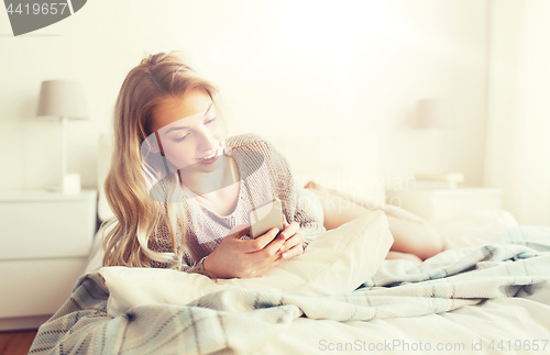 Image of happy young woman with smartphone in bed at home