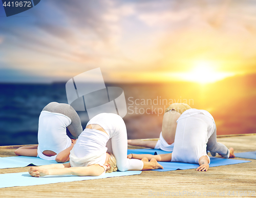 Image of group of people doing yoga pressure pose outdoors