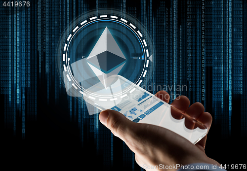 Image of hand with smartphone and ethereum hologram