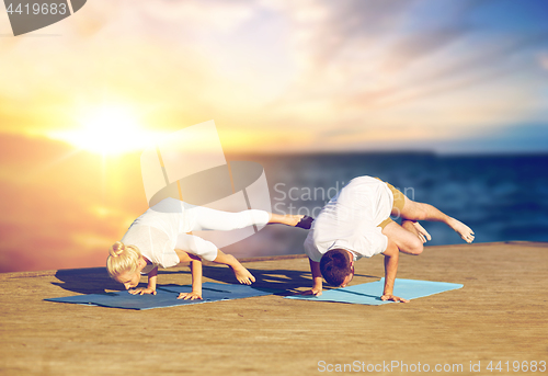 Image of couple doing yoga side crane pose outdoors