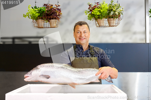 Image of happy male seller holding trout at fish shop