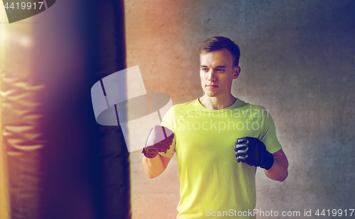 Image of young man in gloves boxing with punching bag