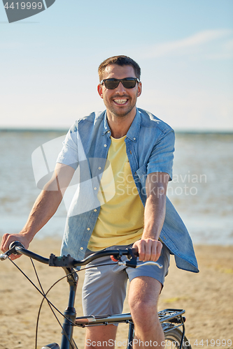 Image of happy man riding bicycle along summer beach