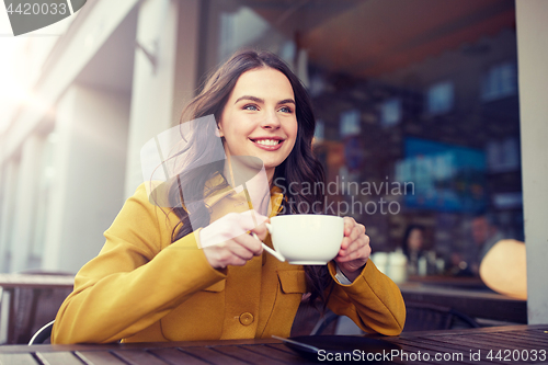 Image of happy woman drinking cocoa at city street cafe