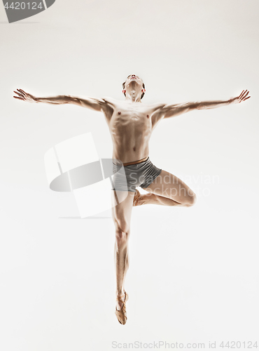 Image of Athletic ballet dancer in a perfect shape performing over the grey background.