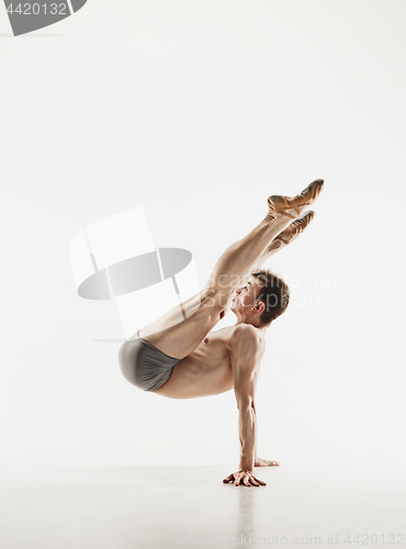 Image of Athletic ballet dancer in a perfect shape performing over the grey background.