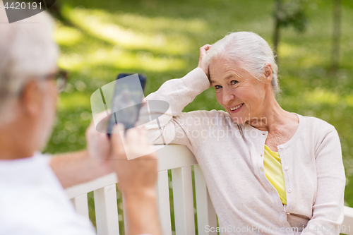 Image of old woman photographing man by smartphone in park