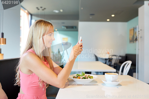 Image of happy woman with smartphone eating at restaurant