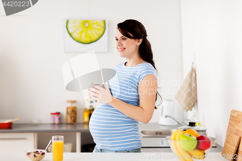 Image of happy pregnant woman with cup at home kitchen