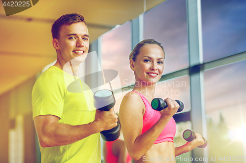 Image of smiling man and woman with dumbbells in gym