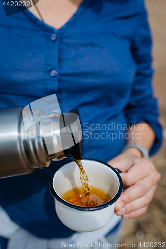 Image of Woman pouring hot tea from a thermos on a sandy beach on a Sunny day. Close up.