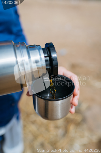 Image of Woman pouring hot tea from a thermos on a sandy beach on a Sunny day. Close up.