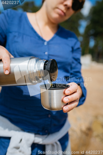 Image of Woman pouring hot tea from a thermos on a sandy beach on a Sunny day. Close up.