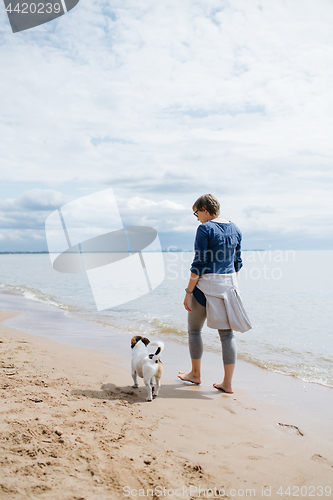 Image of Woman walking with her dog on the sandy beach. Rear view.