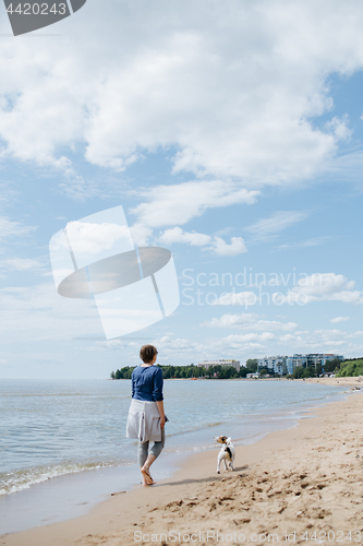 Image of Woman walking with her dog on the sandy beach. Rear view.