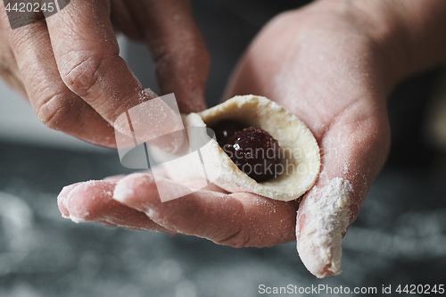 Image of Woman cook manually sculpts dumplings stuffed with cherries