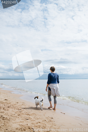 Image of Woman walking with her dog on the sandy beach. Rear view.