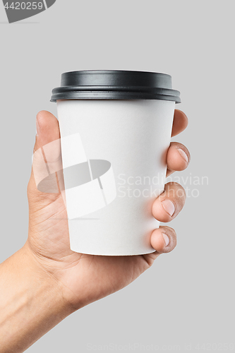 Image of Mockup of men\'s hand holding white paper mid size cup with black cover