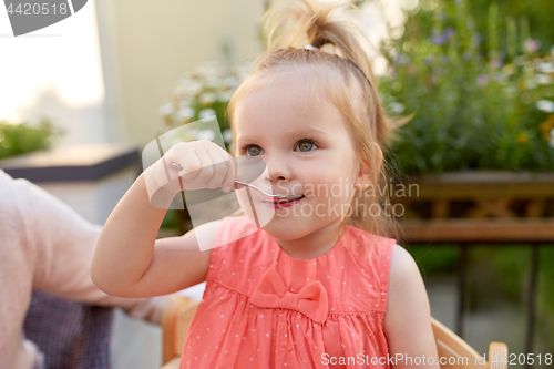 Image of happy little girl with spoon eating outdoors