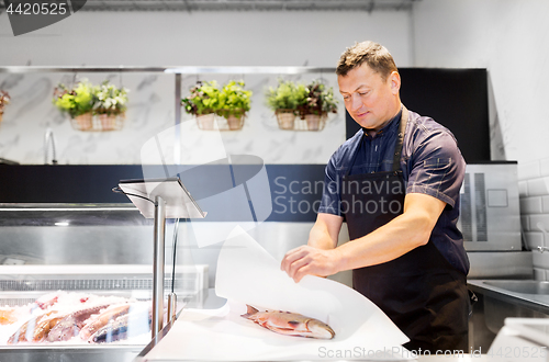 Image of seller wrapping fish into paper at seafood shop