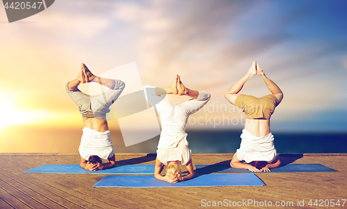 Image of people doing yoga headstand on mat outdoors